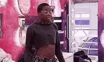 a man wearing a crop top and leopard print shorts is standing in front of a pink wall .