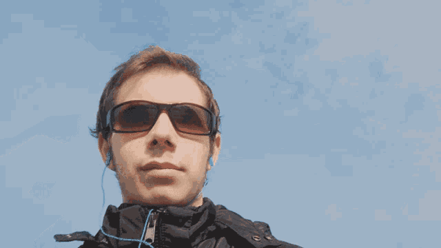 a young man wearing sunglasses and earbuds looks at the camera