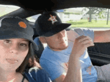 a man and a woman are sitting in a car and the man is wearing a hat with the letter h on it