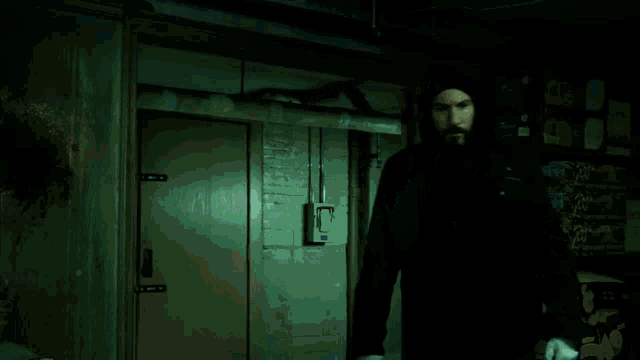 a man in a hooded jacket is standing in a dark room with a light switch on the wall