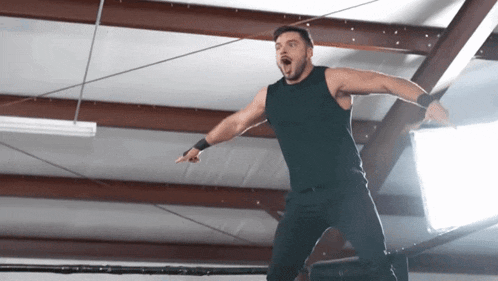 a man in a black tank top and black pants is standing in a wrestling ring
