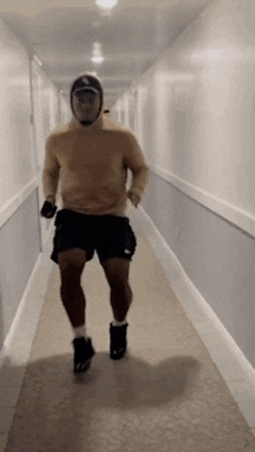 a man is walking down a hallway wearing a hoodie and shorts