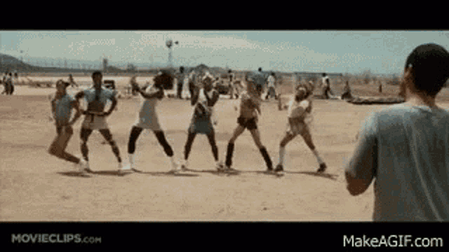 a group of people are playing volleyball on a dirt field while a man watches .