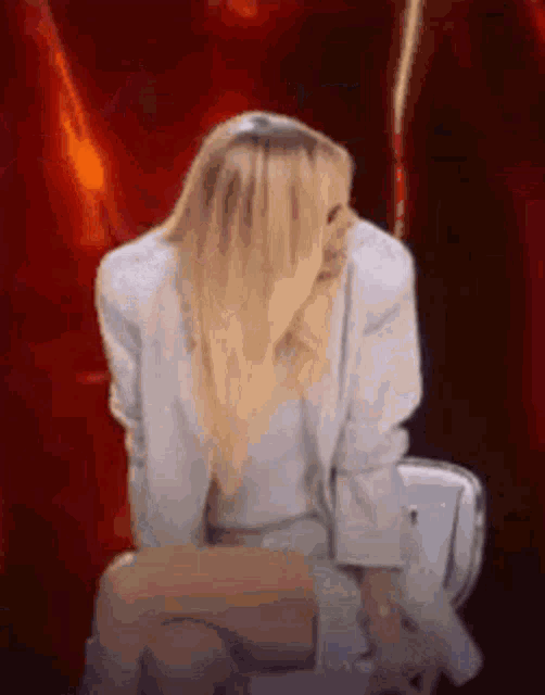 a woman in a white suit is sitting on a toilet with her head down .