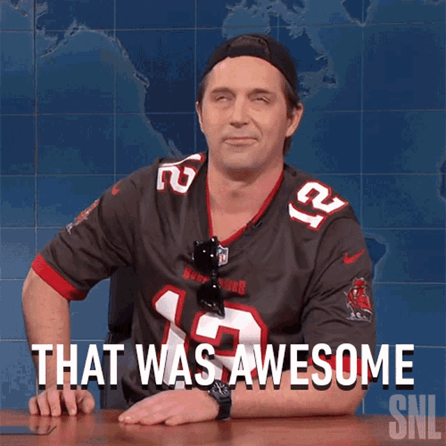 a man wearing a tampa bays jersey is sitting at a table and says that was awesome