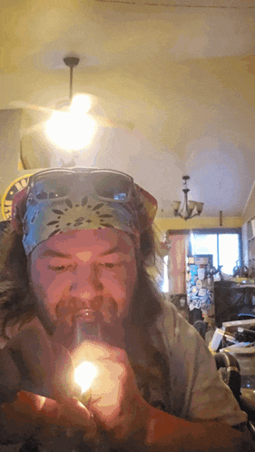 a man wearing sunglasses and a bandana is lighting a cigarette