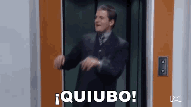 a man in a suit is dancing in an elevator and says quiubo .