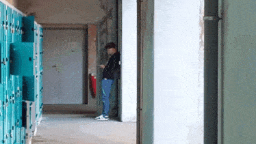 a man is standing in a hallway next to a row of blue lockers .