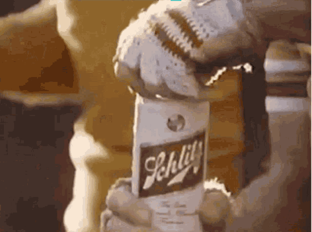 a person is holding a bottle of schlitz in their hand .