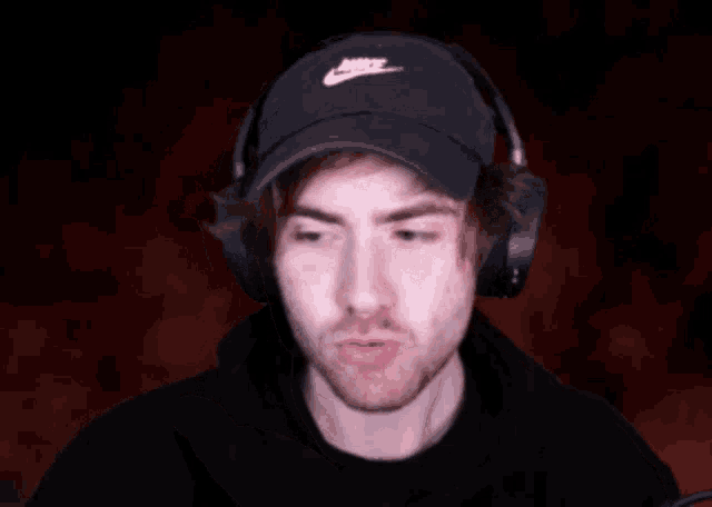 a man wearing headphones and a nike hat is covering his mouth with his hand