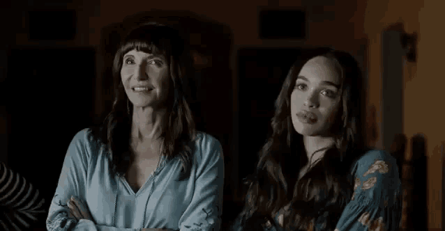 two women are standing next to each other and looking at something . one of the women is wearing a striped shirt .