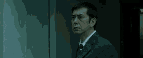 a man in a suit and tie is standing in a dark room and looking down .