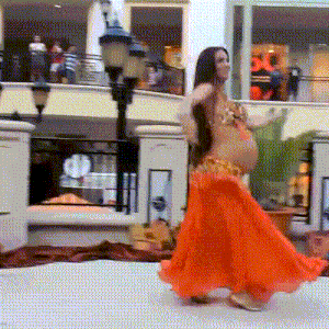 a pregnant belly dancer is dancing in front of a crowd in a mall