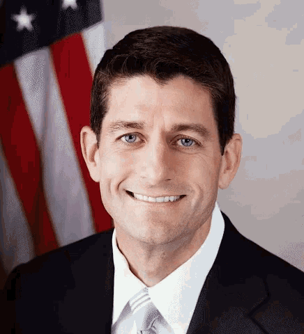 a man wearing a suit and tie smiles in front of an american flag
