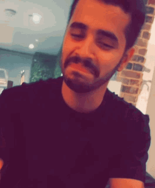 a man with a beard is wearing a black shirt and making a funny face