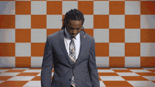 a man in a suit stands in front of an orange and white checkered background