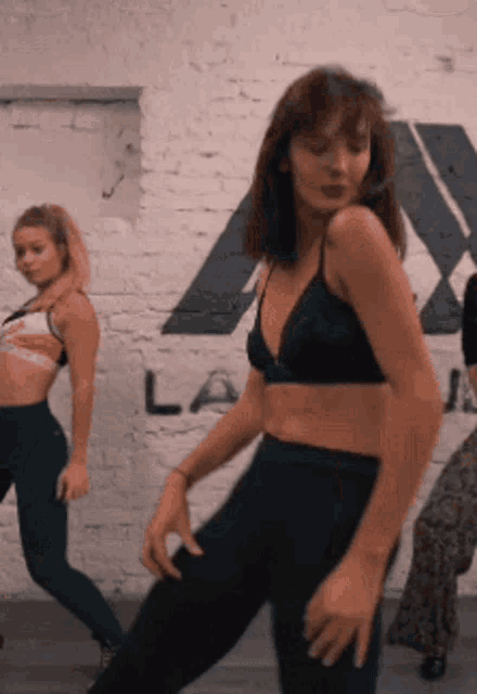 a woman in a black bra is dancing in front of a brick wall with the word la on it