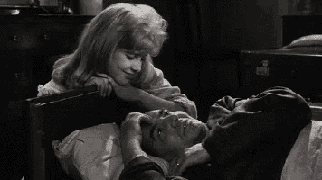 a woman is putting her hand on a man 's forehead while he is laying in bed .