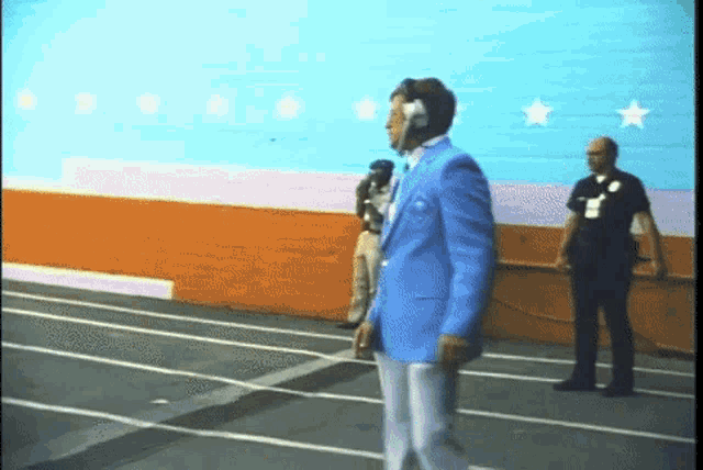 a man in a blue jacket and white pants is walking in front of a wall with stars on it