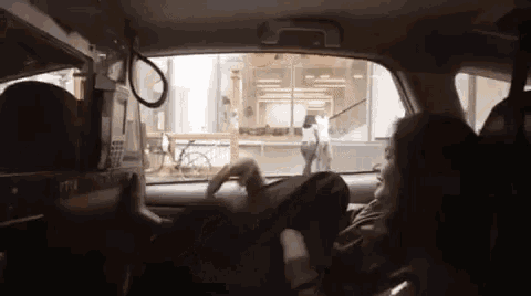 a woman is sitting in the driver 's seat of a car and looking out the window .