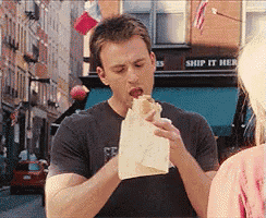 a man is eating a hot dog in front of a shop that says ship it her