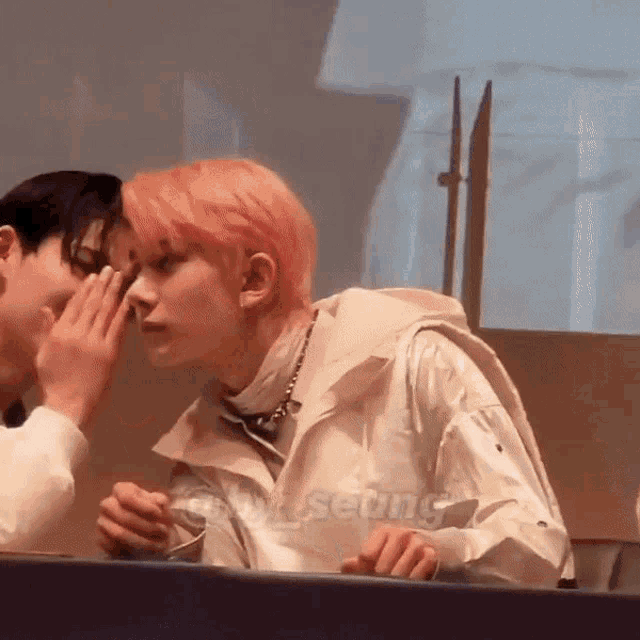 a man whispering into another man 's ear with the word seung on the bottom left