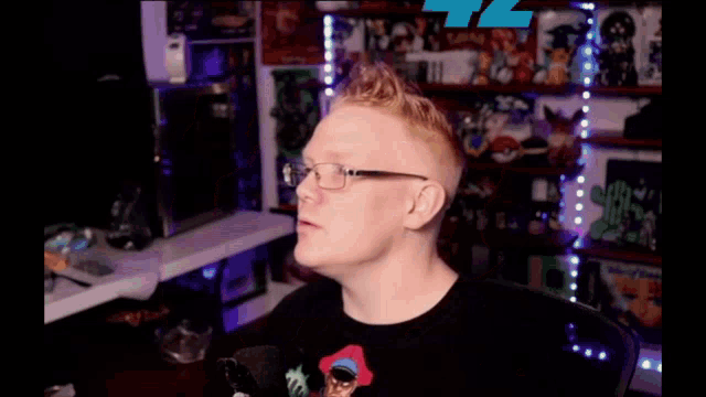 a man wearing glasses and a black shirt is sitting in front of a microphone in a room .