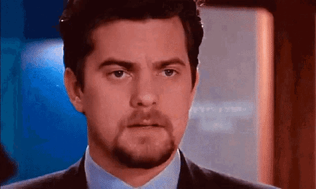 a man with a beard wearing a suit and tie looks at the camera