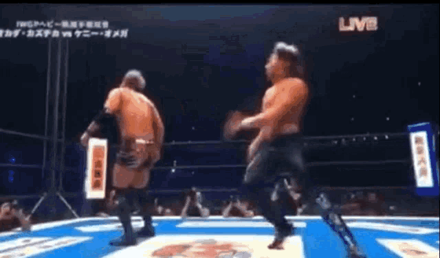 two men are wrestling in a ring with a crowd watching on a live stream .