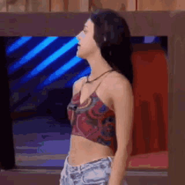 a woman in a crop top and shorts is standing in front of a television screen .