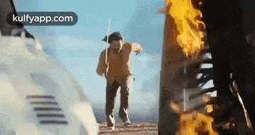 a man is running away from a burning vehicle with a sword .
