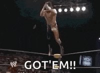 a wrestler is jumping in the air in a wrestling ring while saying `` got em '' .