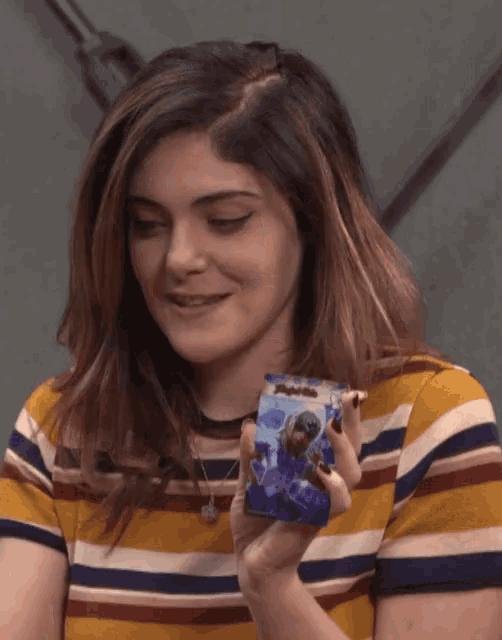 a woman in a striped shirt is smiling while holding a card with a picture of a person on it