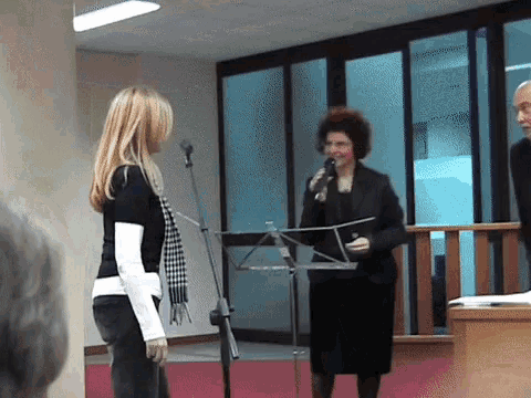 a woman stands in front of a microphone while a man looks on