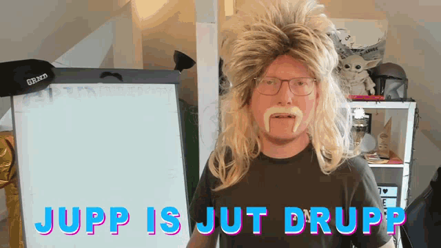 a man wearing a wig and mustache is standing in front of a white board that says jupp is jut drupp