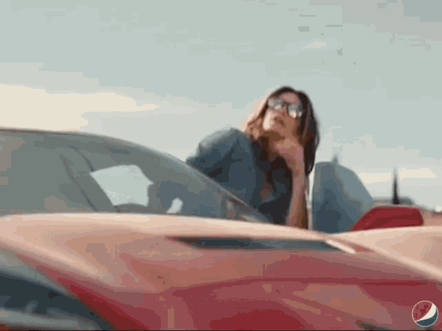 a woman sitting in a red car with a pepsi logo in the background