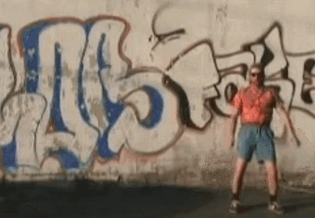 a man is standing in front of a wall with graffiti on it that says " us "