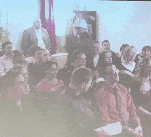 a group of people are sitting in a room with a man standing in the background