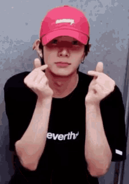 a man wearing a red hat and a black t-shirt is making a heart shape with his hands .
