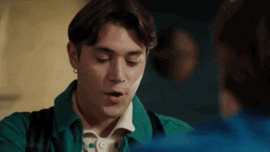 a young man in a green jacket is talking to another man in a blue shirt .