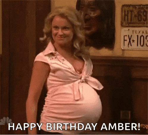 a pregnant woman with a big belly is standing in front of a wall and says `` happy birthday amber '' .