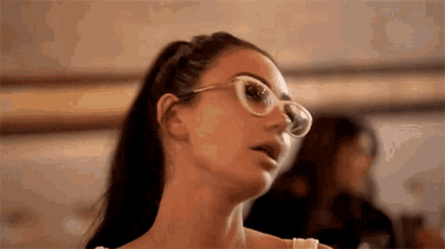a woman wearing glasses and a ponytail is looking up at something .