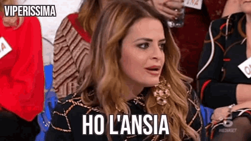 a woman is sitting in a crowd of people and making a funny face and saying ho l' ansia .
