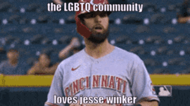 a baseball player wearing a cincinnati jersey stands on the field