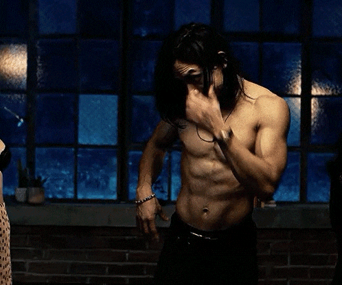 a shirtless man with long hair is standing in front of two women .