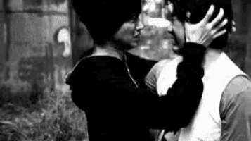 a black and white photo of two men kissing in front of a wall .