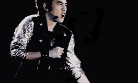 a man in a sequined jacket is singing into a microphone while wearing a headset .