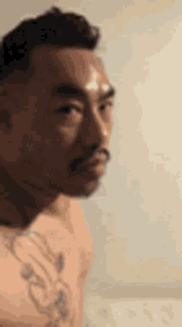 a shirtless man with a tattoo on his arm is looking at something .