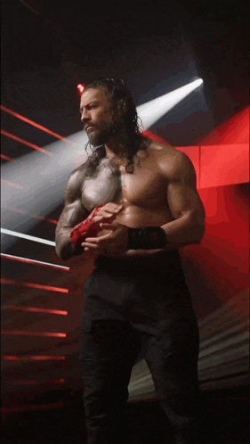 a shirtless wrestler stands in a ring holding a red object