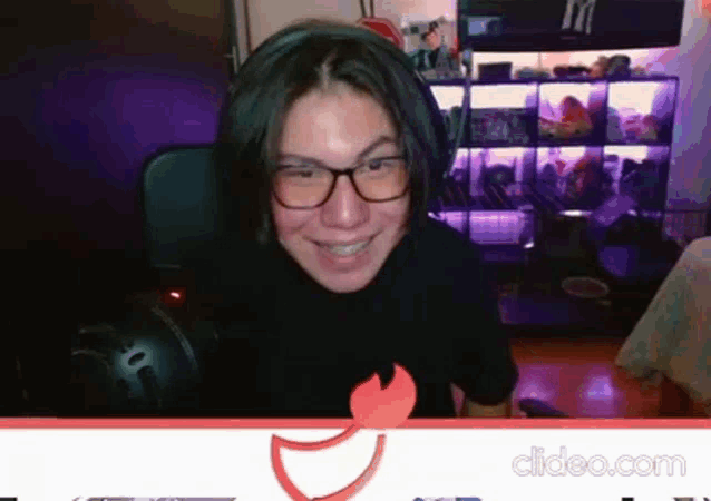 a woman wearing glasses and headphones is smiling while sitting in front of a computer monitor .